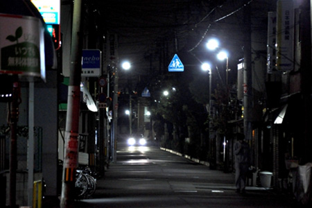 夜の細道に一人の女性と一台の車の光